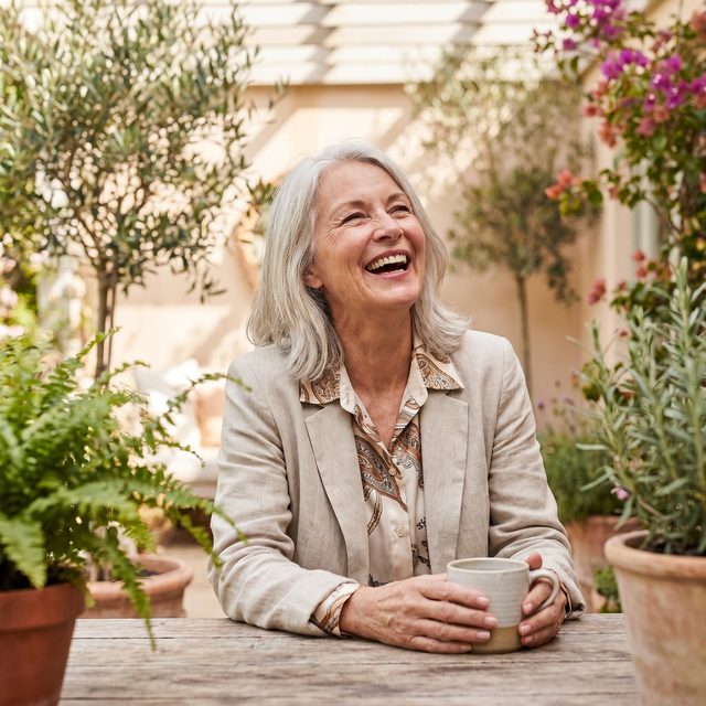 A senior woman laughing joyfully on a sunny patio